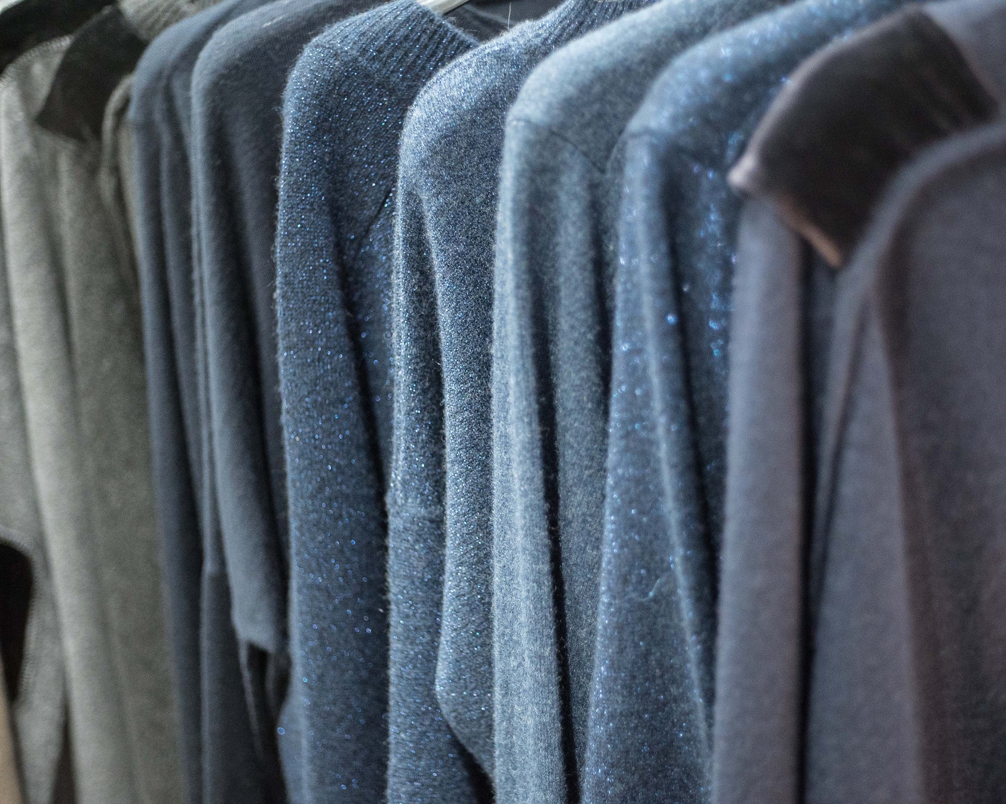 A selection of blue sparkling cashmere wool sweaters hanging side by side on a rail