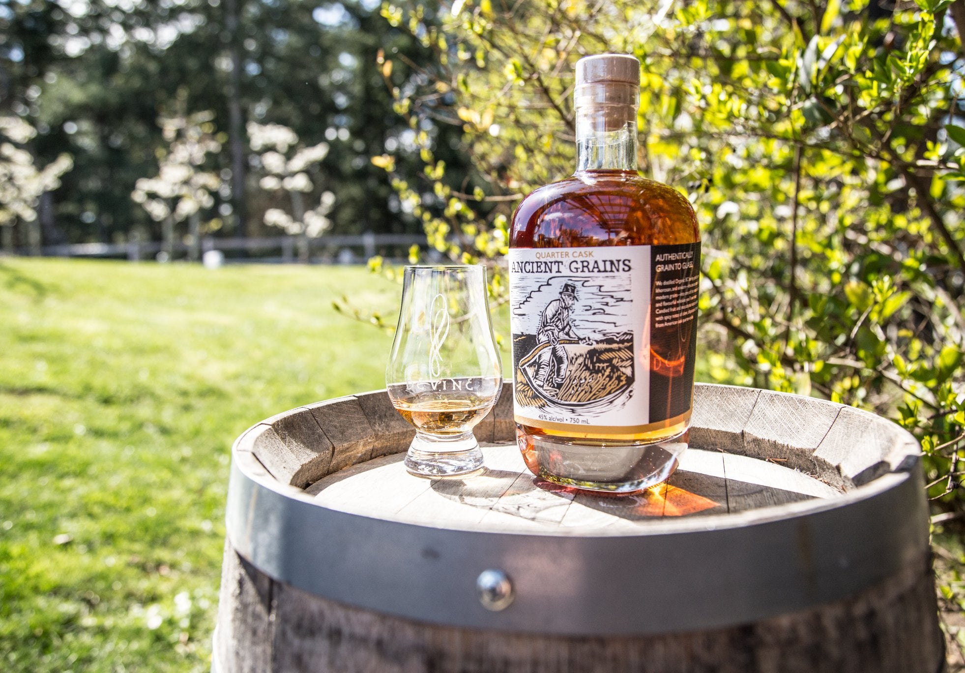 Devine Distillery whisky bottle on a barrel with a Devine whisky tasting glass on a summers day