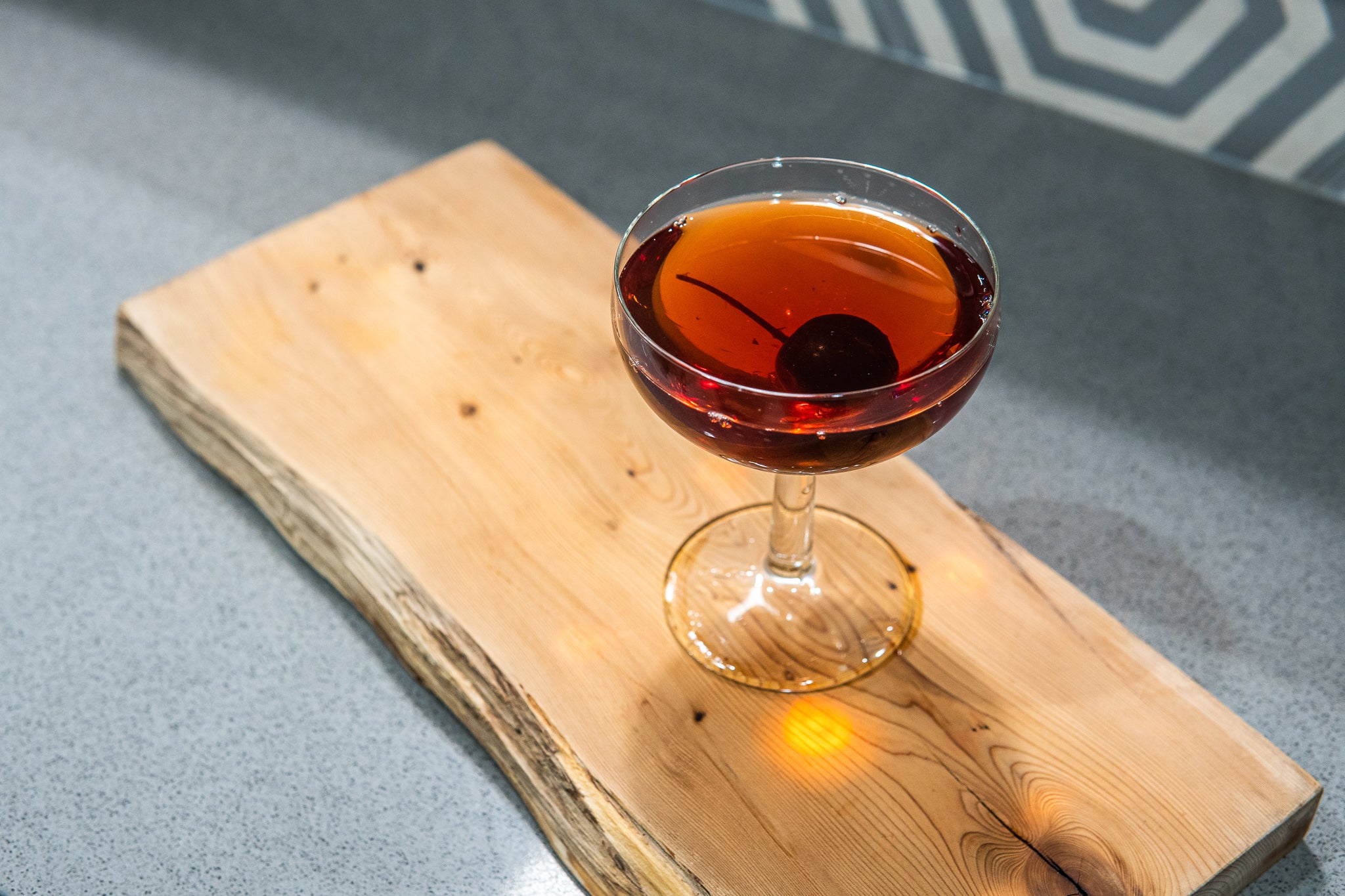 Manhattan cocktail on a wooden board with a cherry sunken to the bottom of the coupe glass