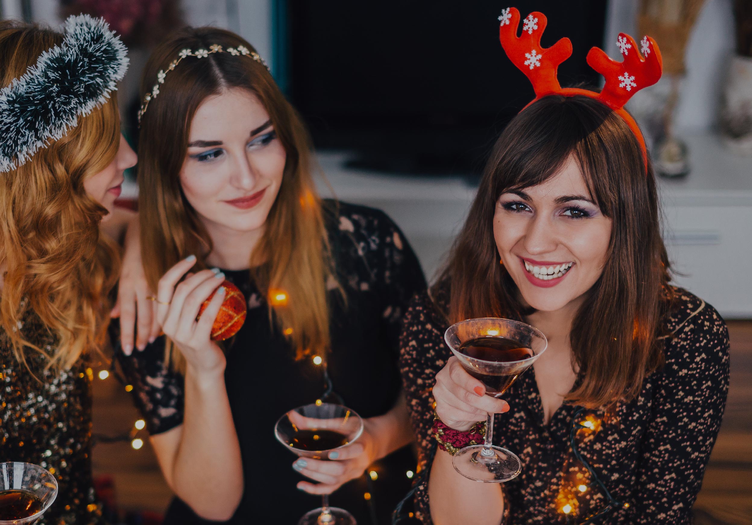 three women drinking bubbly from coupe glasses with red reindeer antlers