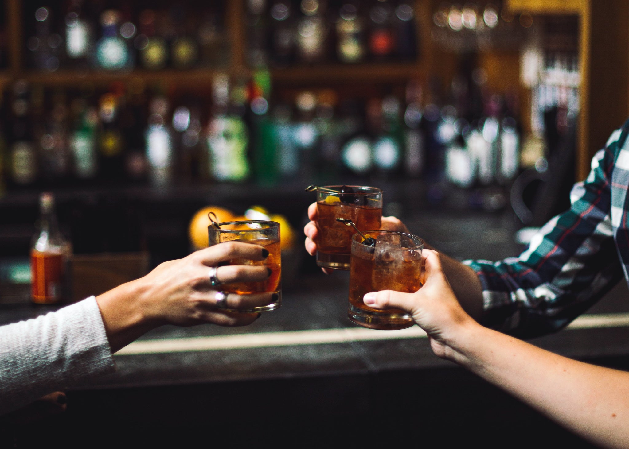 A cheers of three old fashioned cocktails at a bar