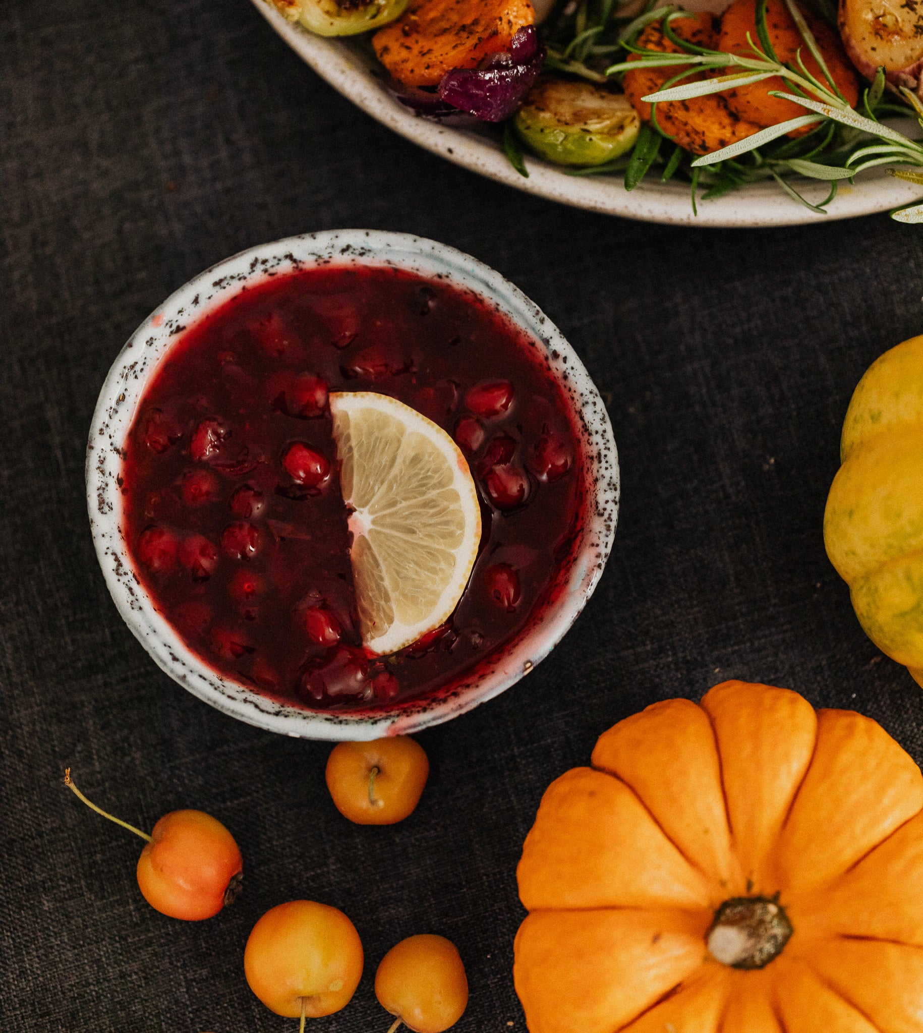 Brandied cranberry sauce in a dish surrounded by cherries, a pumpkin and another side dish