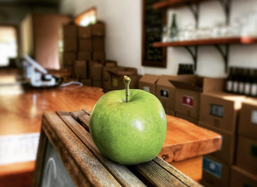 Valley Cider store interior with boxes of ciders lining the walls and a big green apple perched on a chalkboard post