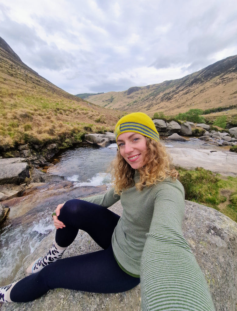 Leanne sitting on a rock wearing FINDRA beanie, fern base layer and leggings