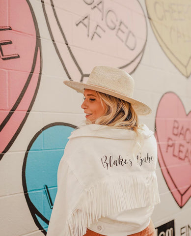 Bride wearing personalized white jacket with fringe in front of iconic candy heart mural in Nashville