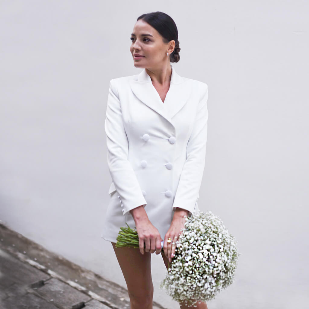 A bride wearing a Christina Devine bridal trench coat holding flowers 