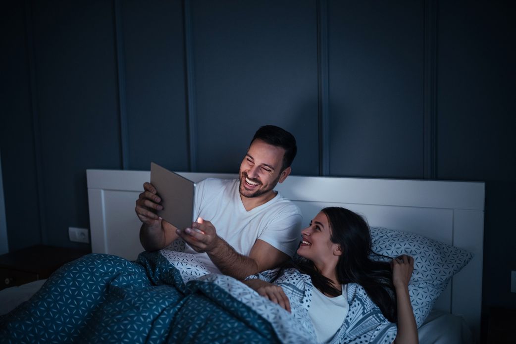 young couple watching a movie on their tablet while in bed at night