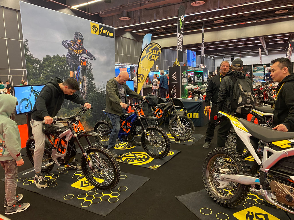 People sitting on Surron electric bikes at a motorcycle show.