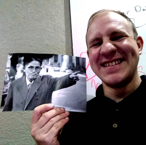 A close up of Mr. Corey holding a black and white photographs with his right hand while smiling to the camera
