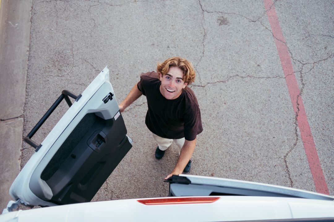 Skateboarder Dylan Jaeb looks up at the camera while standing behind a van
