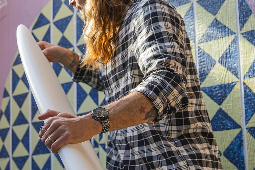 Surfer wearing a Nixon Sentry Chrono watch while handling his surfboard.