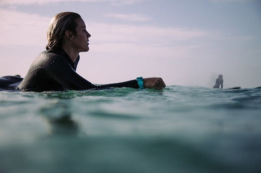 A surfer paddles out into the ocean wearing a Nixon waterproof watch