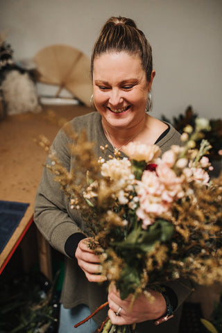 Main St Blooms owner, Rachel is smiling as she arranges some flowers into a bouquet