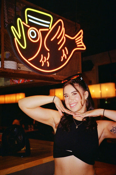 Photograph of a person smiling next to a neon sign