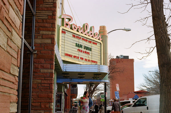 Photograph of person holding flowers walking down street past music venue