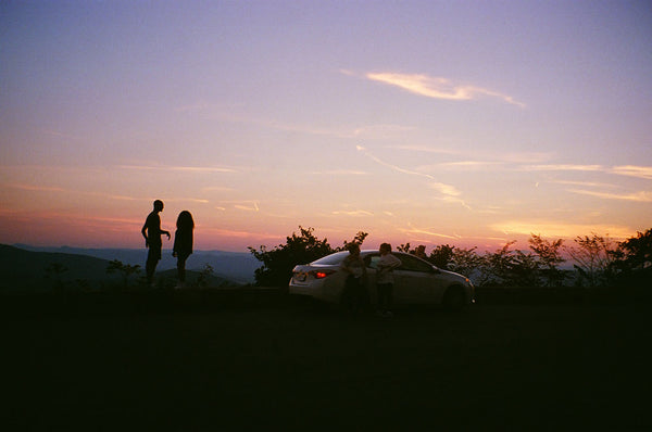 Photograph taken at dusk of a car and people on top of a mountain