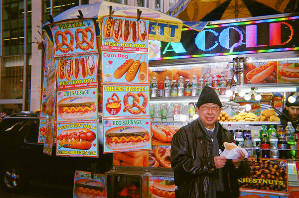 Photograph of person holding a hot dog by a food truck in a city