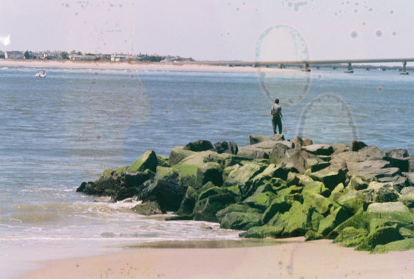 Photograph of person standing on rocks near the ocean