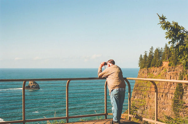 Photograph of man looking through binoculars at ocean vista