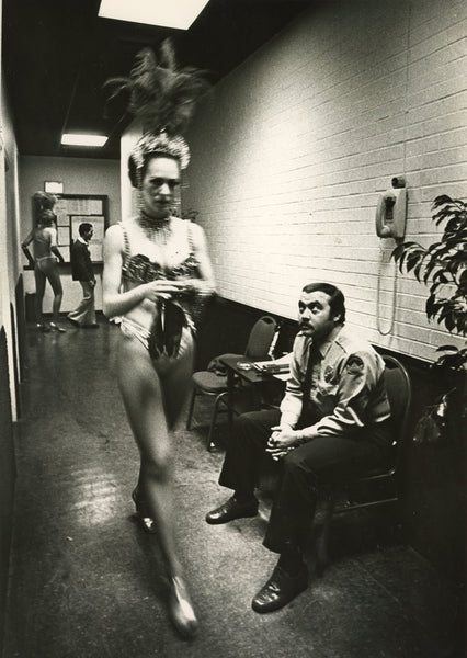 Photograph of dressed up woman walking backstage as security person watches her walk by