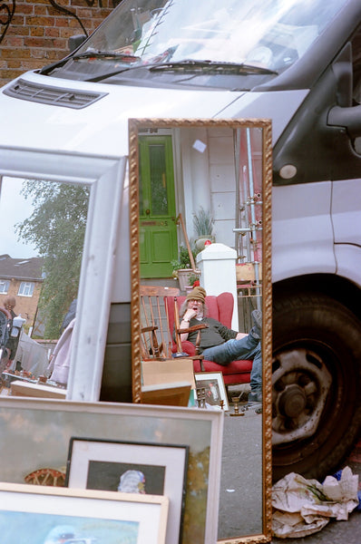 Photograph of man's reflection in mirror propped against car