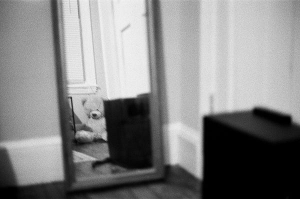 Photograph of a reflection of a stuffed bear sitting in a corner