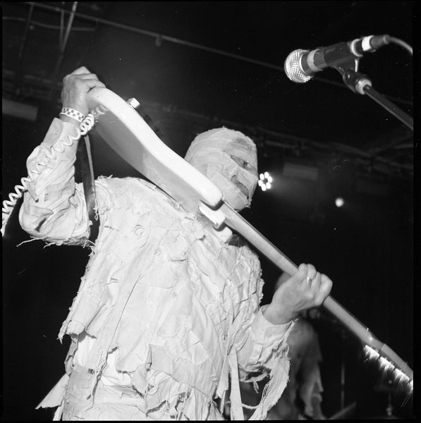 Photograph of band member dressed in a mummy costume holding a guitar