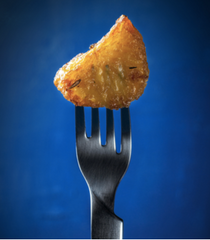 Dramatic arty shot of a single roast potato on a fork against a dark blue background