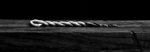 A rope incense on its side on a piece of lumber in front of a black backdrop.