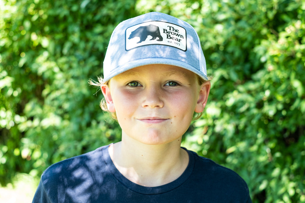 Boy wearing a blue trucker style hat with words the brown bear