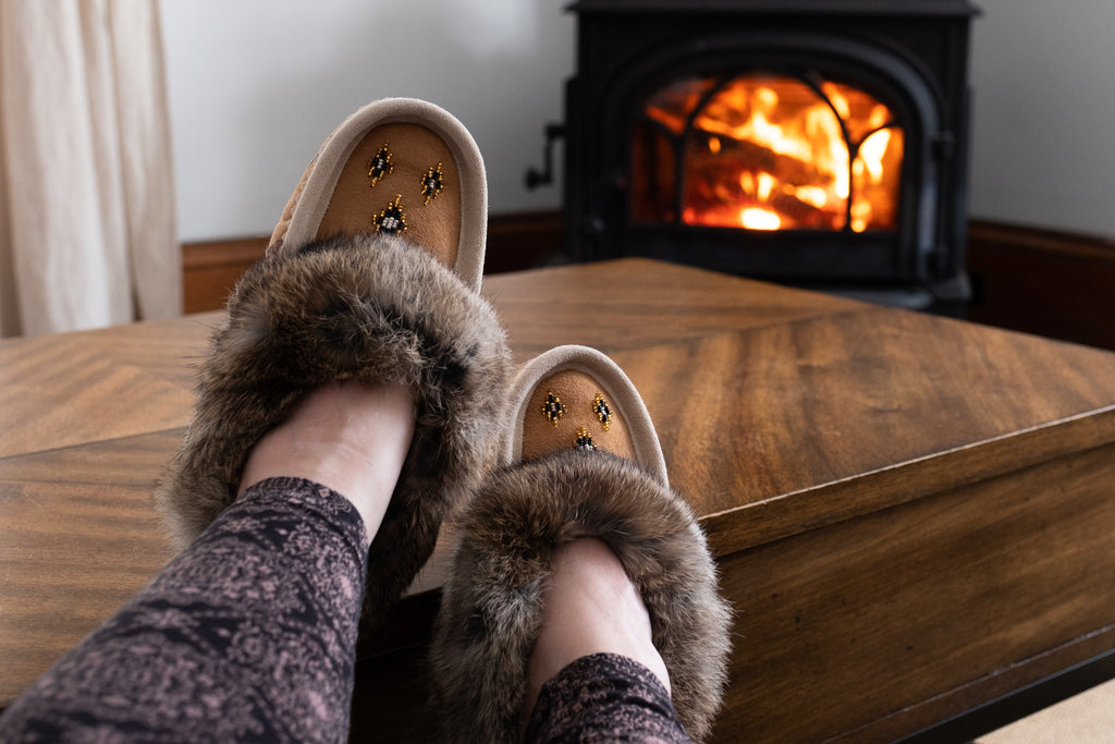 Resting feet on a coffee table with fire in background wearing a pair of moccasin slippers