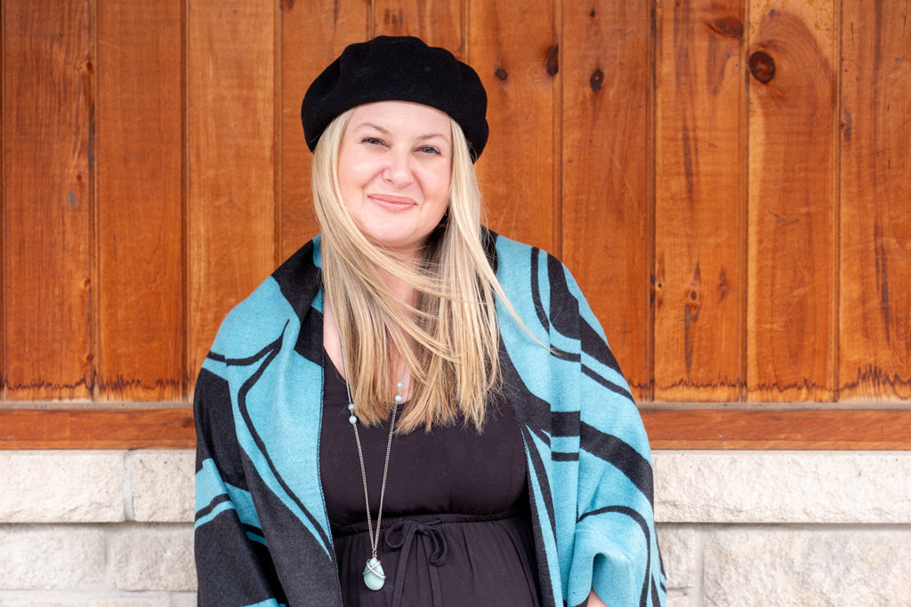 Woman wearing a black beret hat and a warm blue reversible fashion cape and turquoise necklace