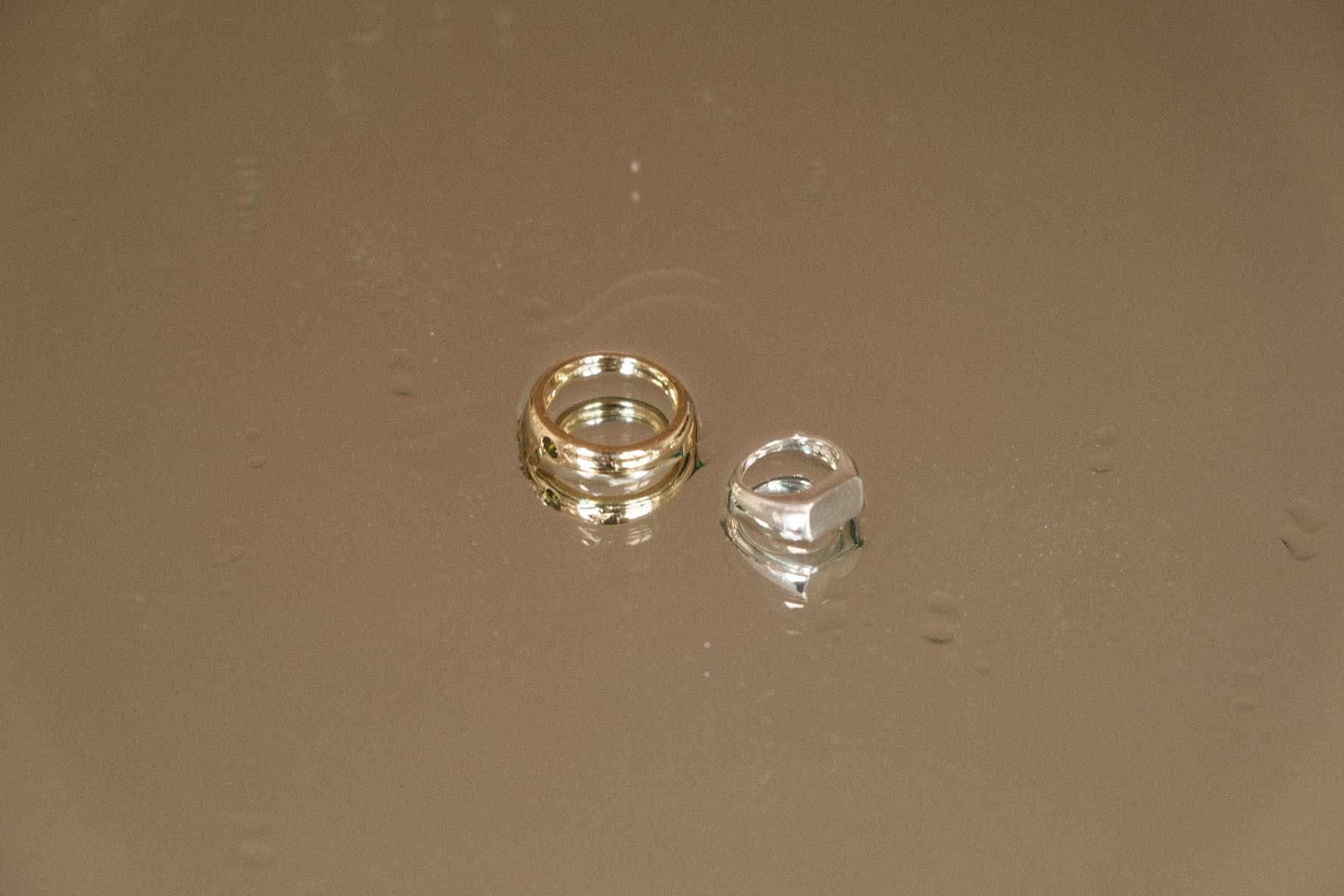 Image of a 14k gold ring and sterling silver ring sprinkled with water droplets