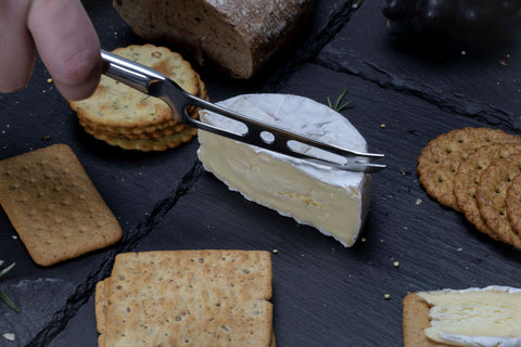 Soft cheese knife cutting through brie on a cheese board