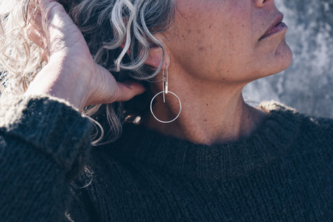 An image of a model wearing the circle hoop earring dangling from a cast sterling silver bar.