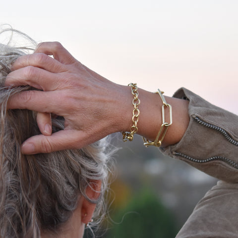 An image of a model wearing two 18k gold chunky chain bracelets, stacked together.