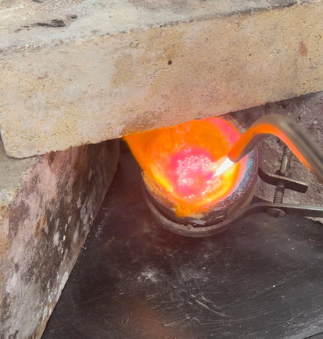 Image of Liz using a torch to melt metal in a crucible to pour it into an ingot.