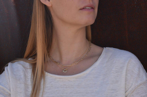An image of a model wearing a layered necklace look that features a larger paperclip chain paired with a delicate chain with a lost wax pendant. This look is featured in buttery 18k gold.