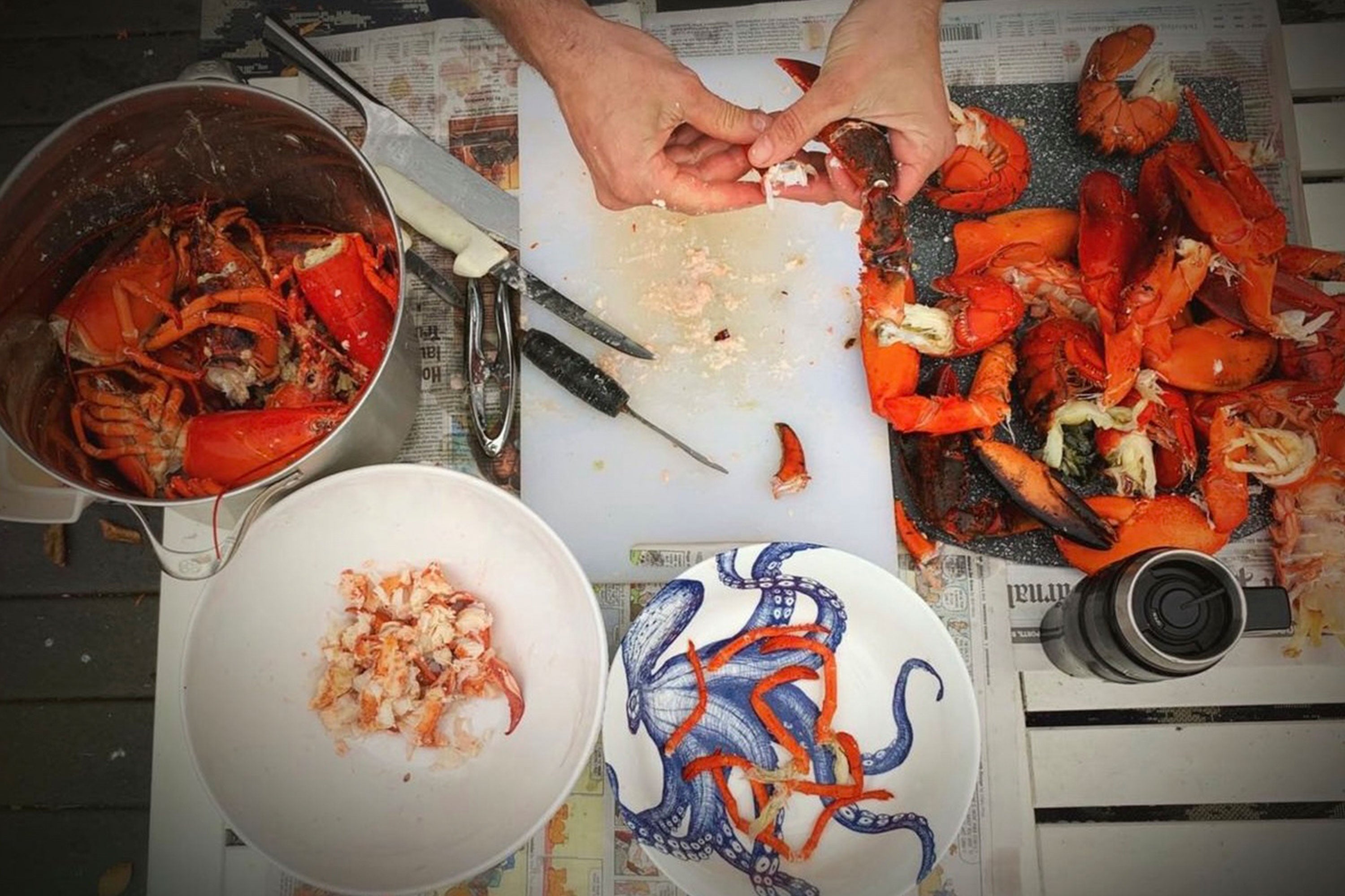 Above view of lobster casserole being prepared on a table with knives, plates, a chopping board and pan visible