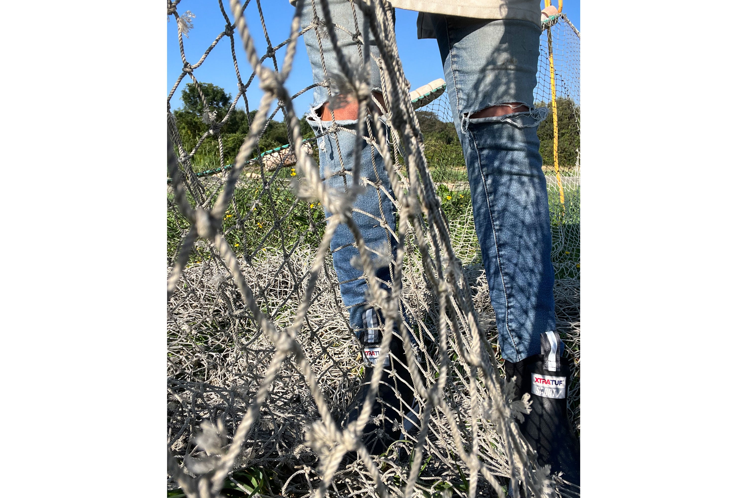 Close up of Corey Forrest repairing a fishing net, wearing a pair of jeans and a pair of black Xtratuf Ankle Deck Sport boots