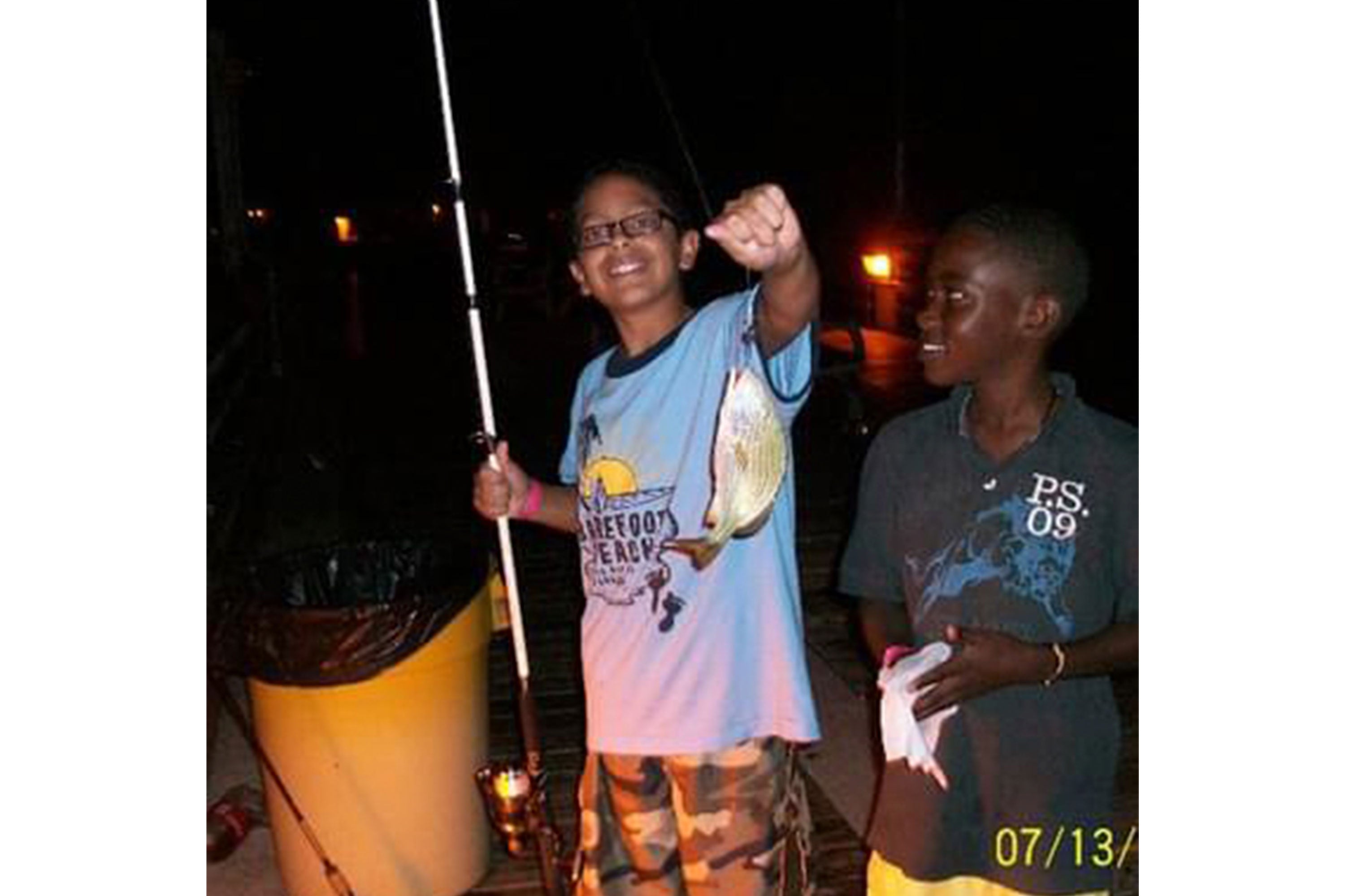 Emmanuel and a friend fishing at night with friend showing a fish caught on his line