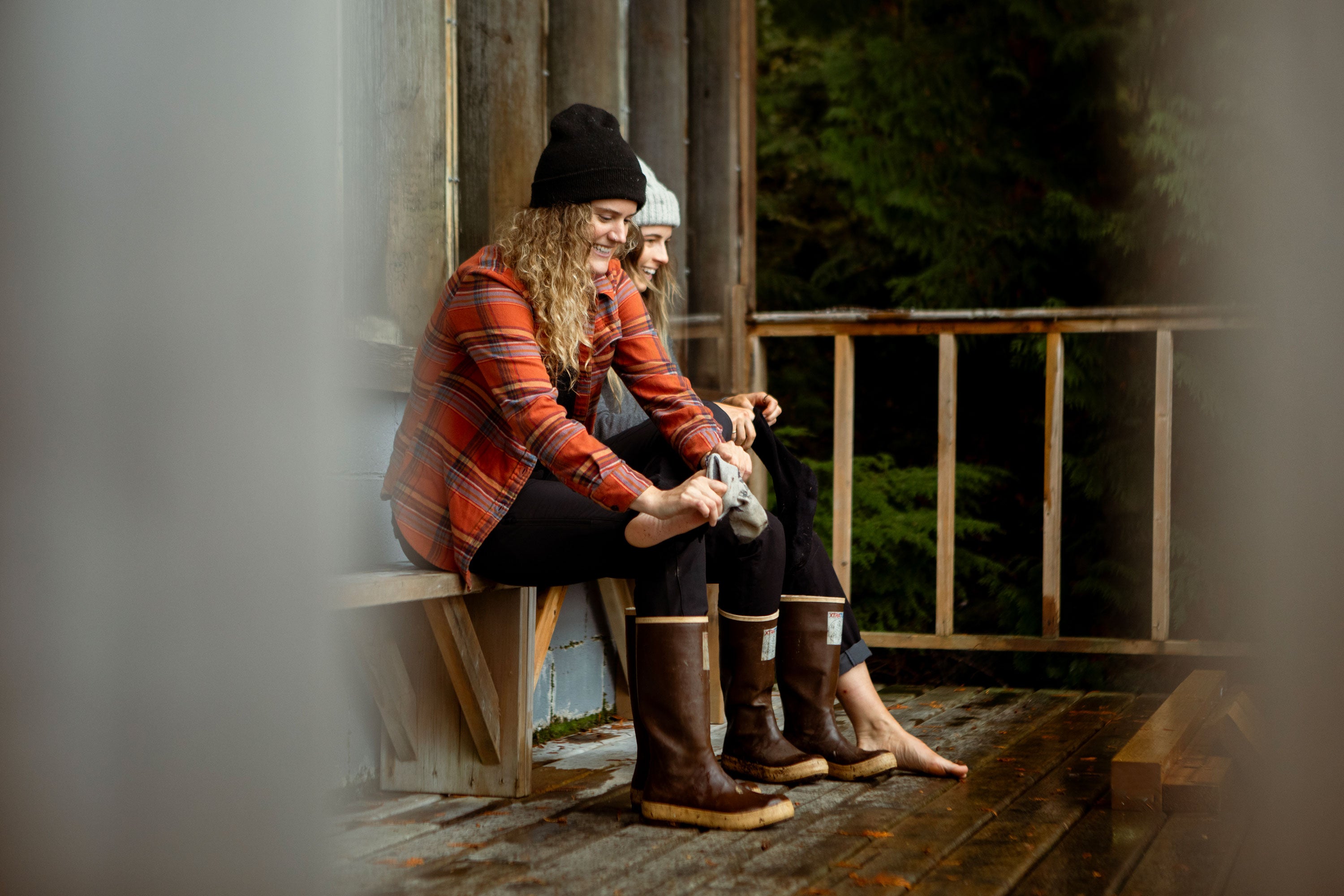Two women sat on a wooden porch, putting on socks and Xtratuf Legacy Boots