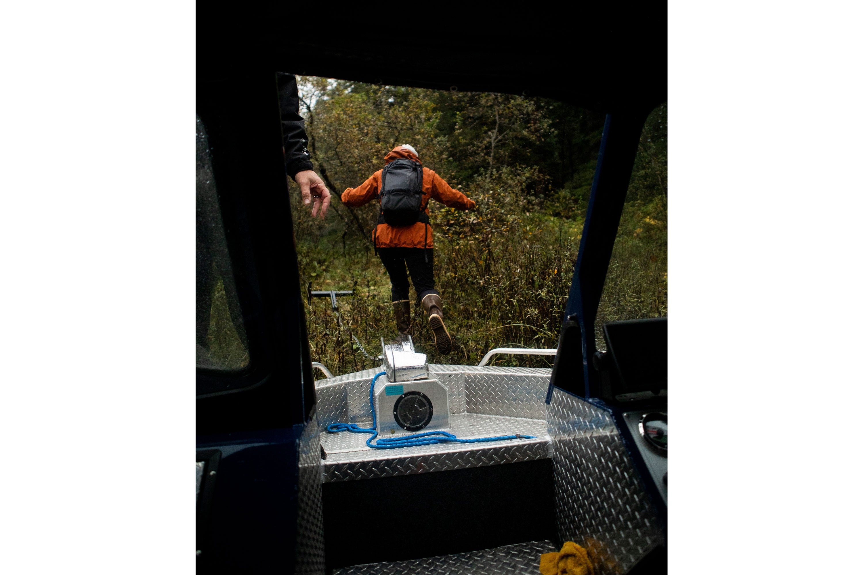 Person jumping off the back of a boat, wearing a backpack, orange waterproof jacket and pair of Xtratuf Legacy Boots