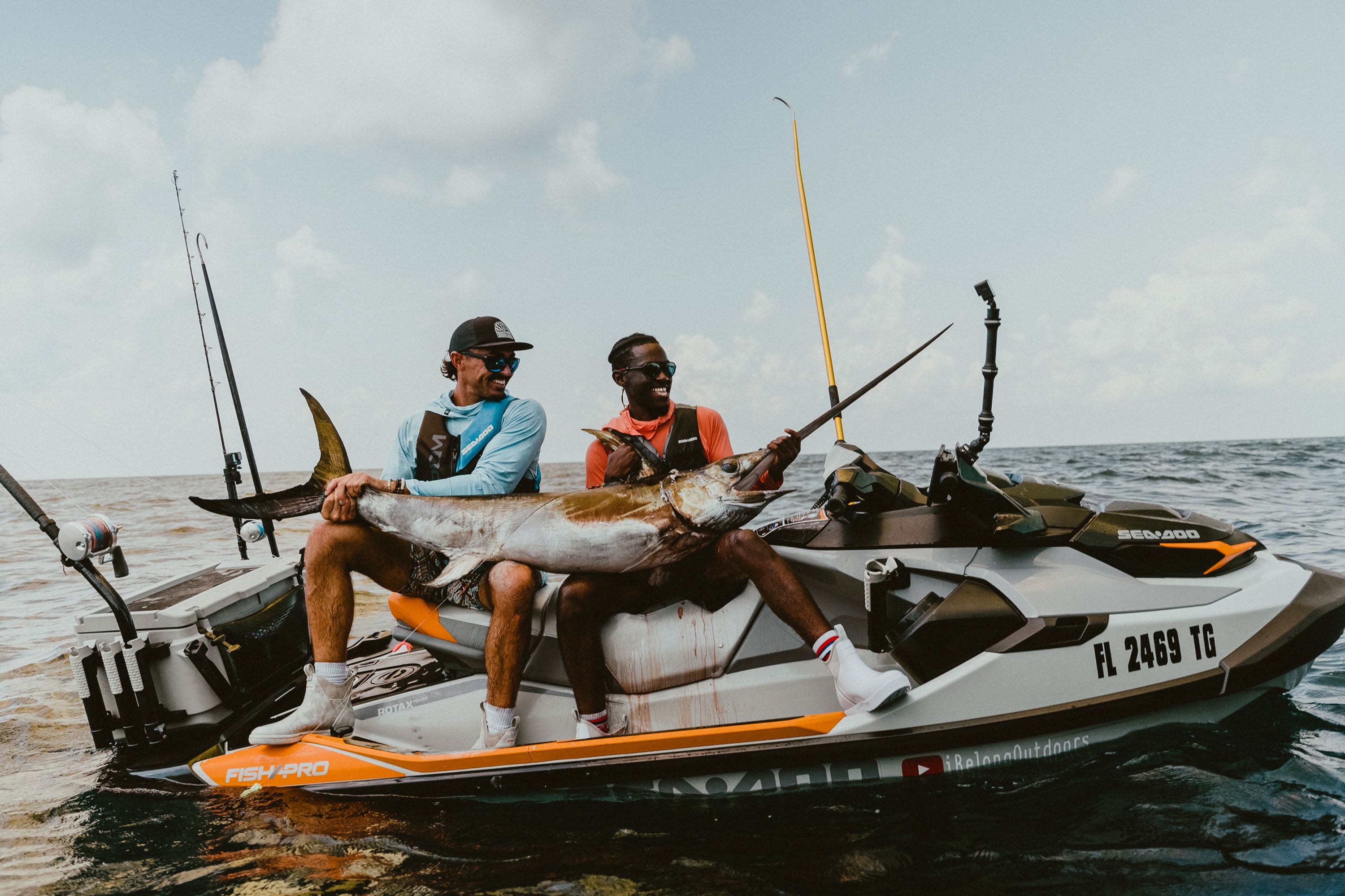 Emmanuel sitting with another man on a jet ski smiling as they hold a large swordfish