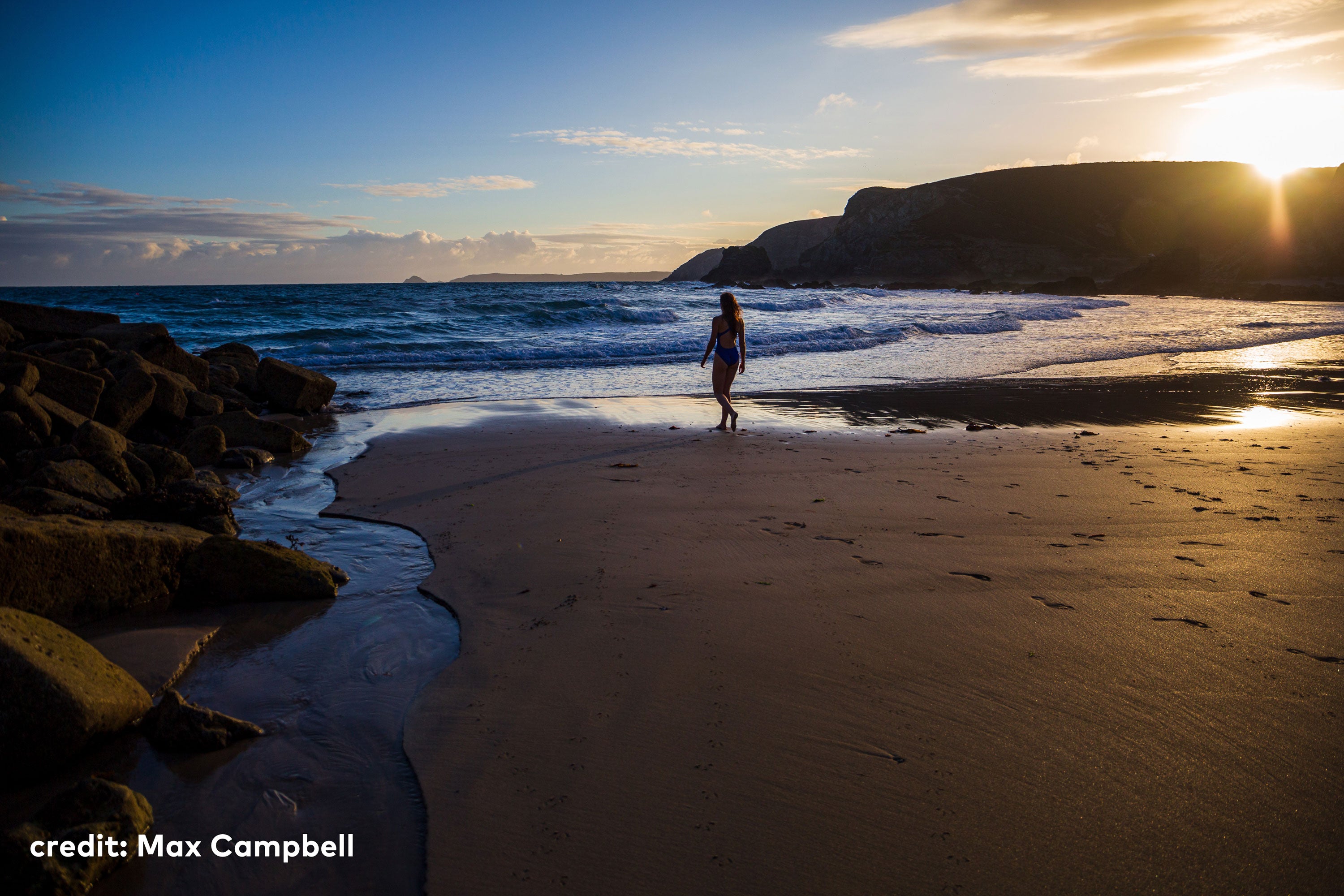 A woman waking towards an incoming tide on the beach at sunset