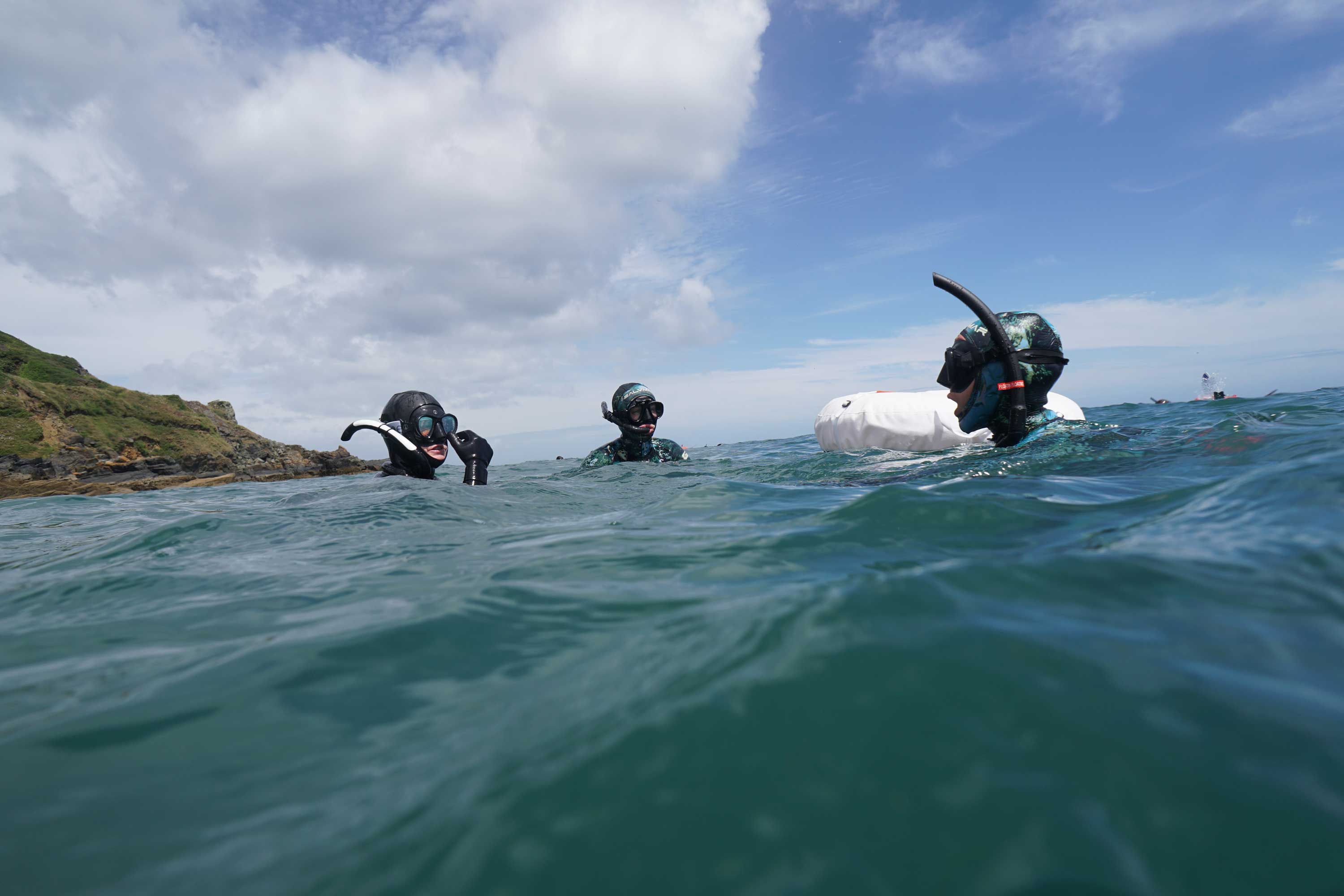 Three people with their heads out of the water, wearing scuba masks and snorkels