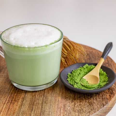 Matcha beverage on a wooden table next to Match Powder and a wooden spoon against a plain background in Australia