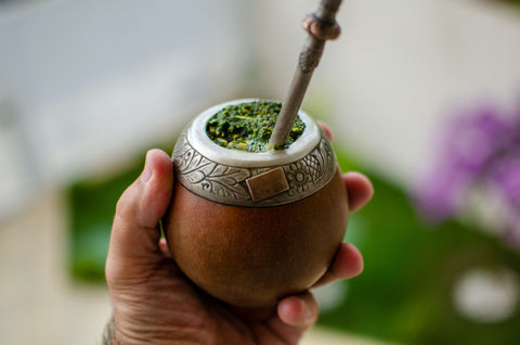 Person holding South American gourd filled with Yerba Mate, complete with a bombilla straw inserted inside