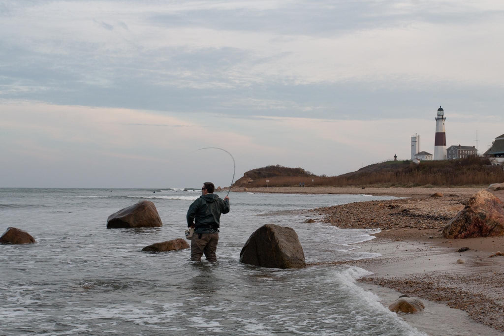 Man surf fishing on a beach near a lighthouse