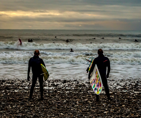 Two surfers standing on the edge of the incoming tide.